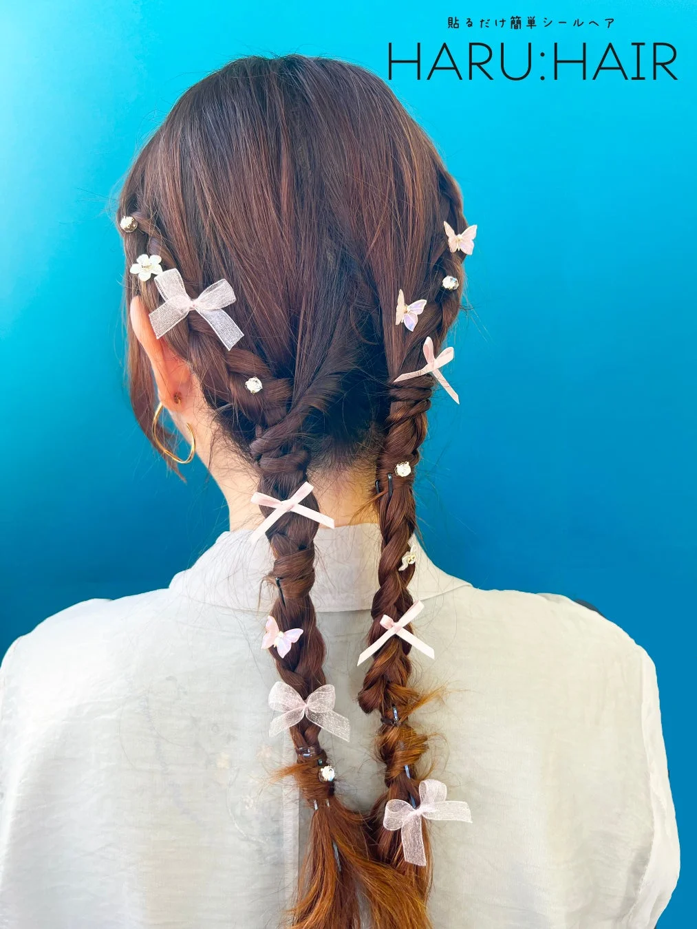 鮮やかな青い背景の前で、女性の後ろ姿が写っています。髪は三つ編みにされ、小さなピンクのリボン、蝶々、きらめくジュエルで可愛らしく飾られています。