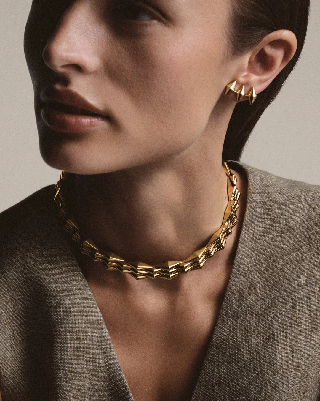 ジオメトリックなデザインのゴールドネックレスとピアスを身につけた女性