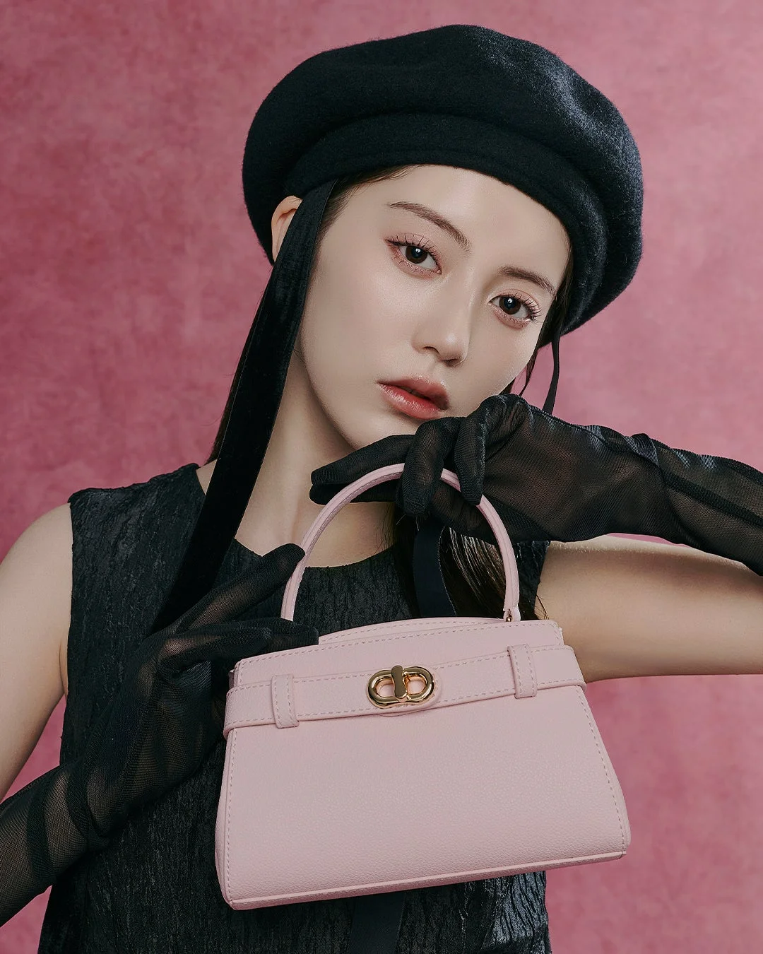 黒いベレー帽とシアーグローブを身につけた女性が、ピンクのハンドバッグを手にカメラを見つめているポートレート