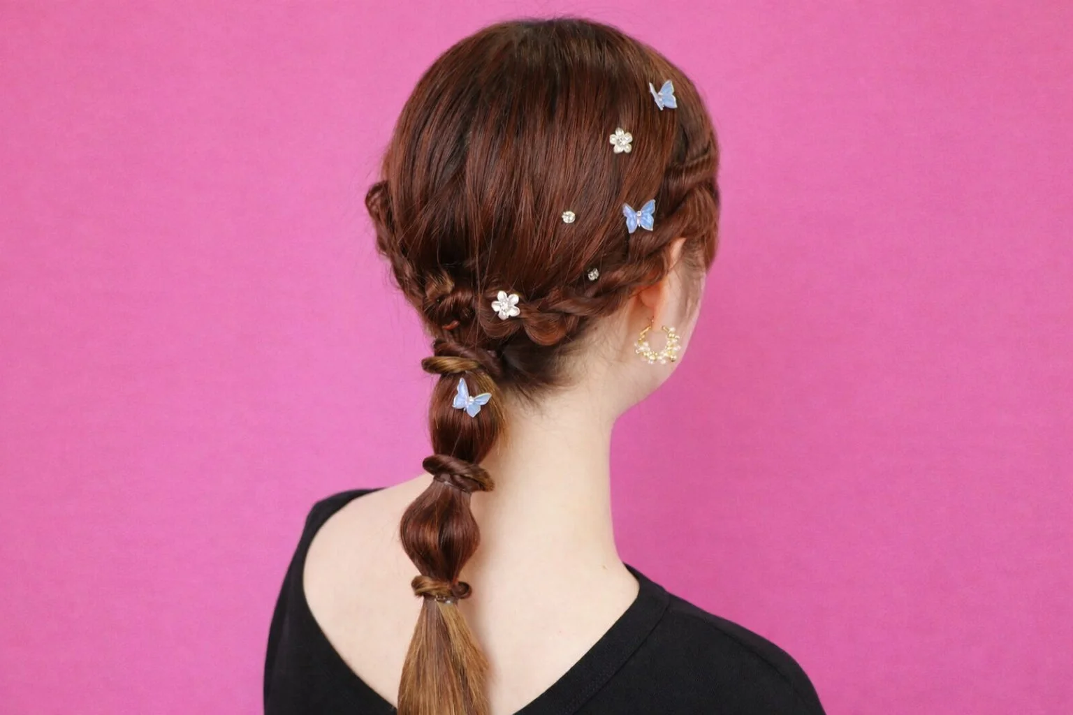 鮮やかなピンクの背景をバックに、編み込みとバブルポニーテールのヘアスタイルをした女性の後ろ姿です。髪には蝶や花の形をした可愛らしいヘアクリップが飾られています。おしゃれでフェミニンな印象です。