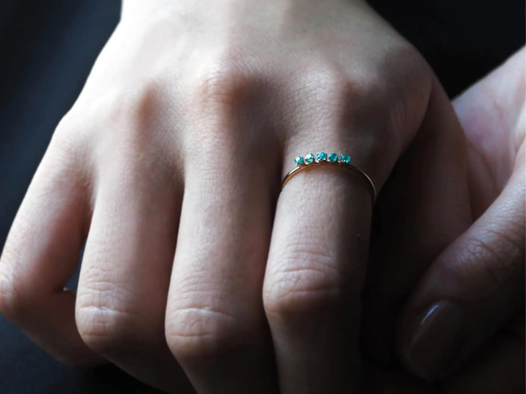 華奢な指に、複数の小さな青緑色の宝石があしらわれたゴールドの指輪