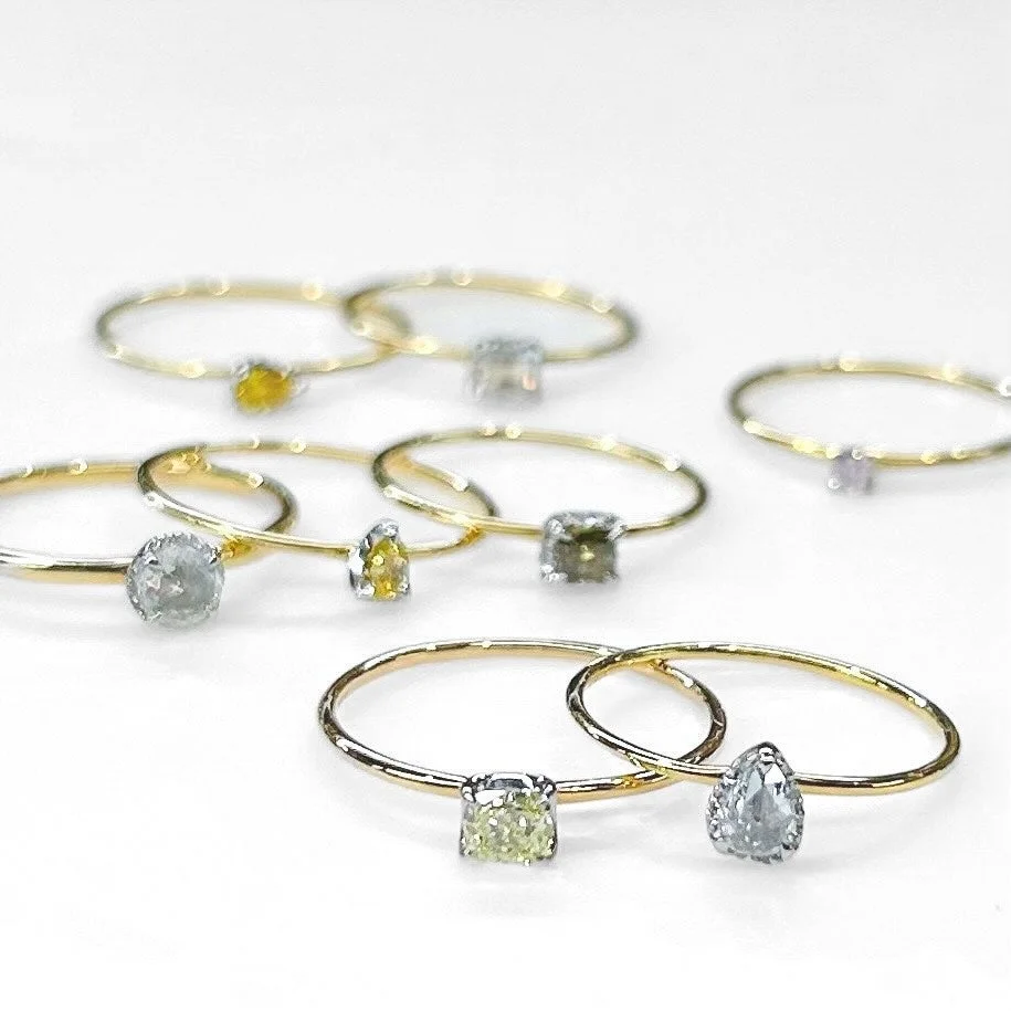 白い背景に、様々な色とカットの天然ダイヤモンドがあしらわれた華奢なゴールドリングが複数並べられています