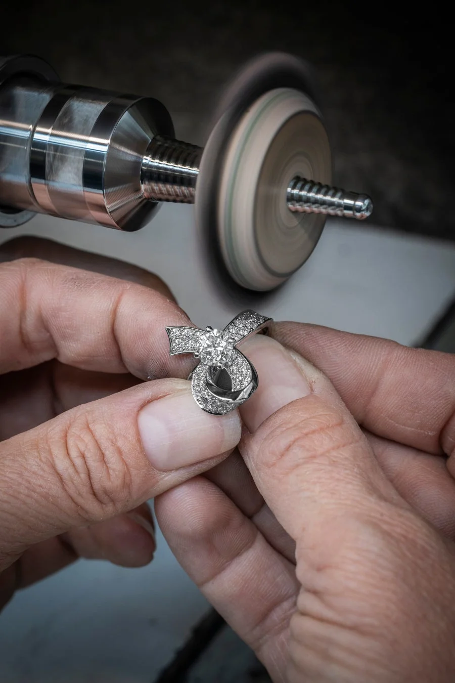 職人の手がダイヤモンドが散りばめられた美しいジュエリーを研磨機の前で丁寧に扱っている様子です。細部までこだわり、輝きを引き出す宝飾品の製造過程を捉えた一枚。