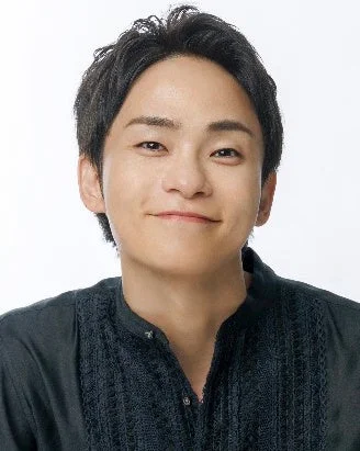 白い背景の前で、黒い襟なしシャツを着た若い男性が微笑んでいます。親しみやすい表情でカメラを見つめています。