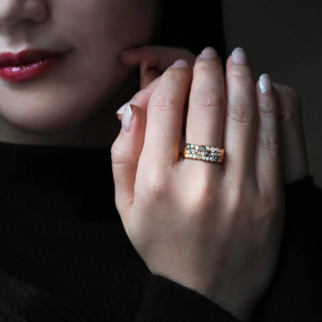 黒い服を着た女性の手元を写した画像。薬指にはカラフルな宝石が散りばめられたゴールドの指輪