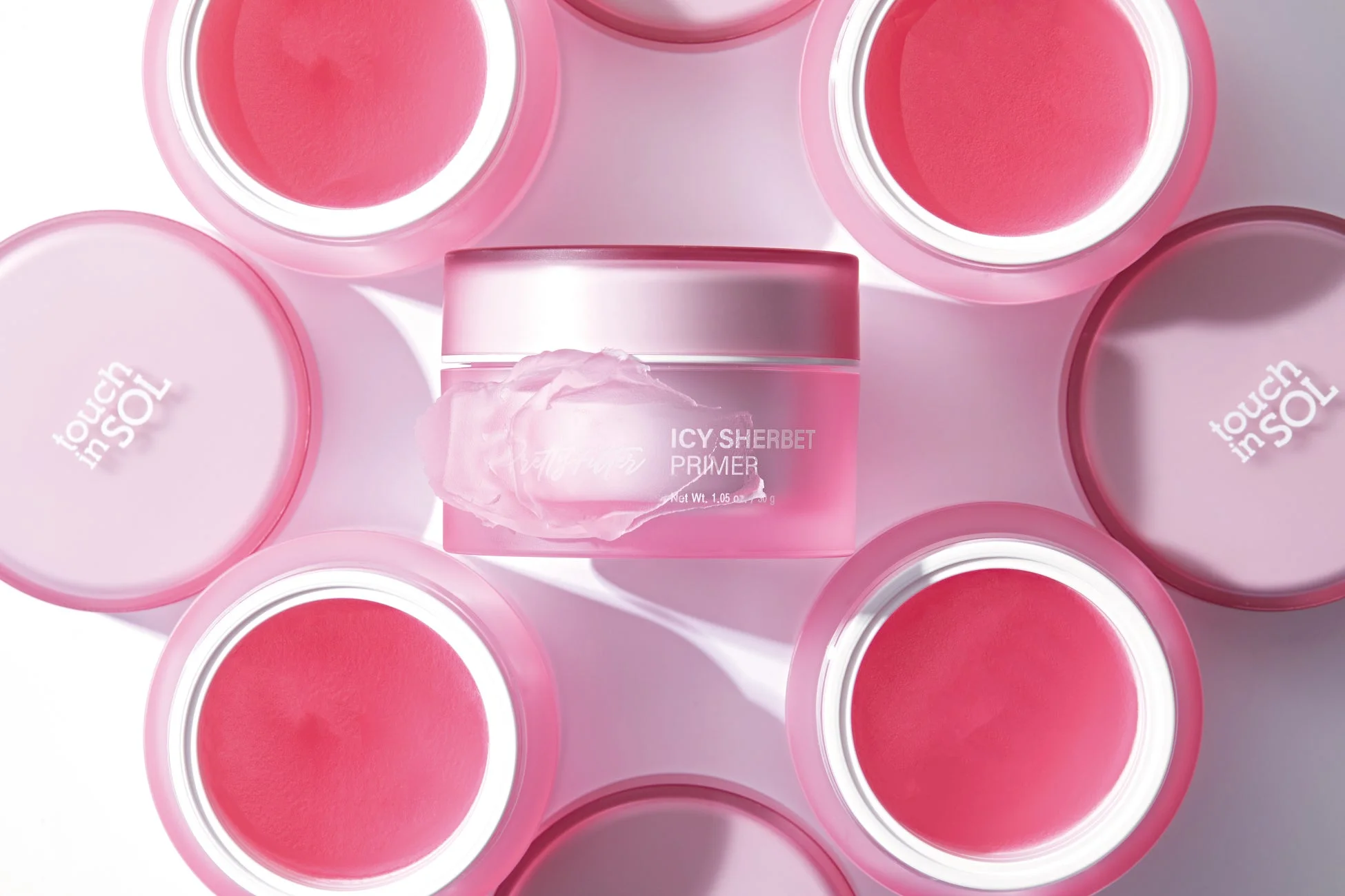 ピンク色の化粧品容器が多数配置されており、中央には「ICY SHERBET PRIMER」と書かれたプライマーがクリーム状の内容物とともに写っています。周囲の容器は蓋が開けられ、中身のピンク色のジェルが見えています。全体的に明るく清潔感のあるビューティー製品のイメージです。