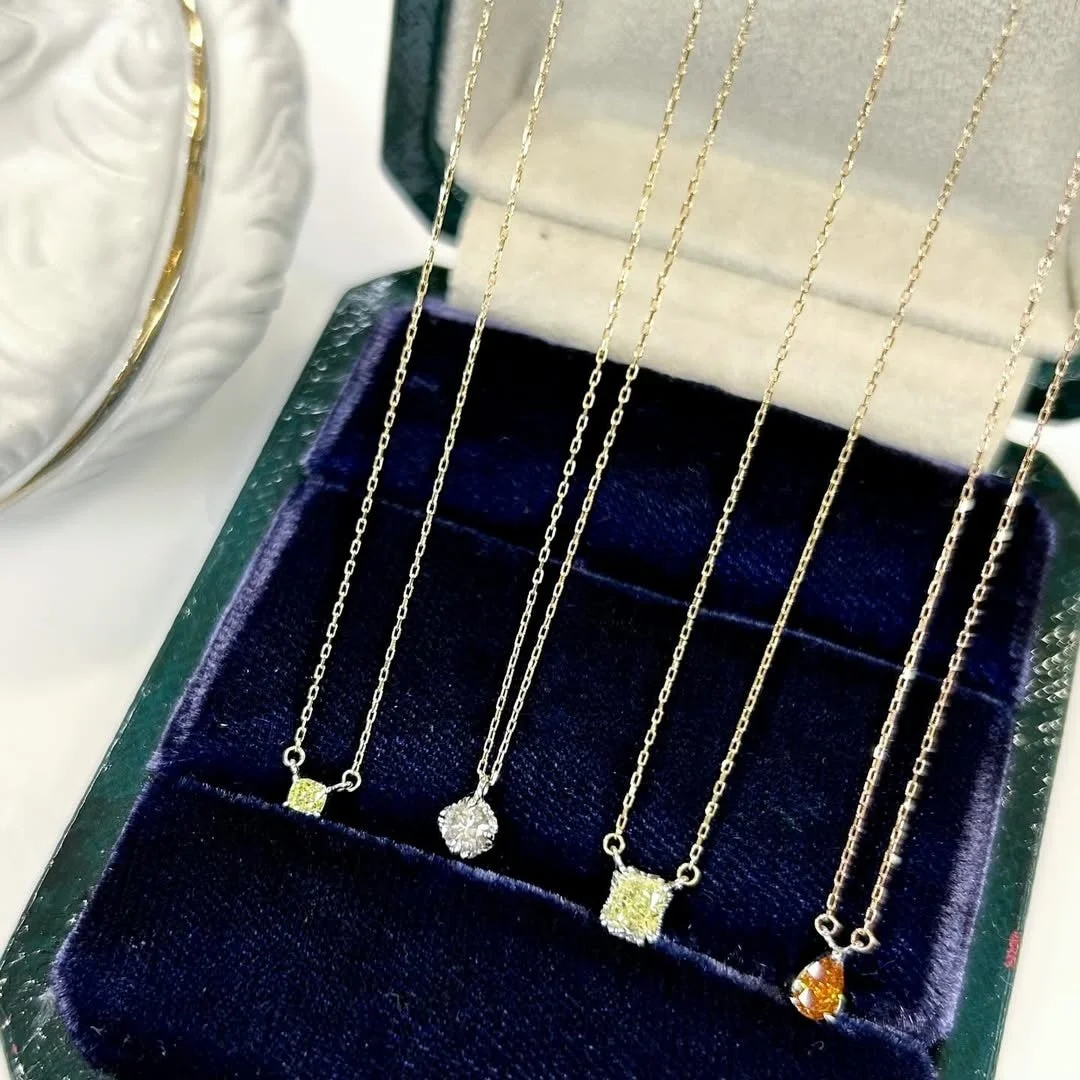 濃い青色のベルベットのジュエリーボックスに、イエロー、クリア、オレンジなど様々な色と形の宝石が付いた繊細なゴールドネックレスが4本並べられています