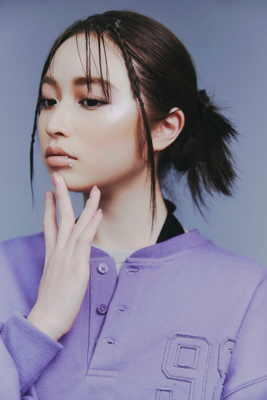 パープルのスウェットを着た若い女性のポートレート。リップピアスや顔のデコレーション、個性的なヘアスタイルが特徴的で、クールな雰囲気を醸し出しています。