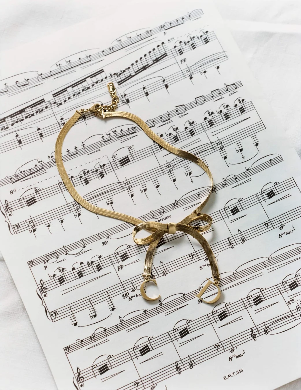 金色のスネークチェーンネックレスがリボンのように結ばれCDチャームが付いたデザイン