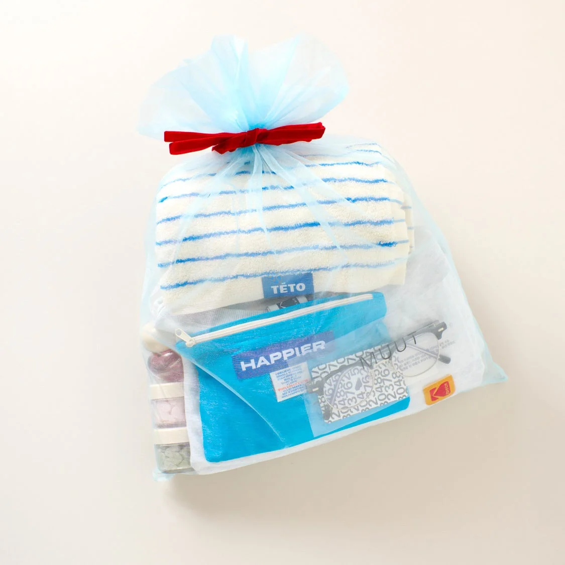 青いオーガンジーのギフトバッグに、ストライプ柄のタオル、青いポーチ、眼鏡、いくつかの小物がきれいに詰め合わせられています。赤いリボンがアクセントの、プレゼントや贈答品にぴったりのセットです。